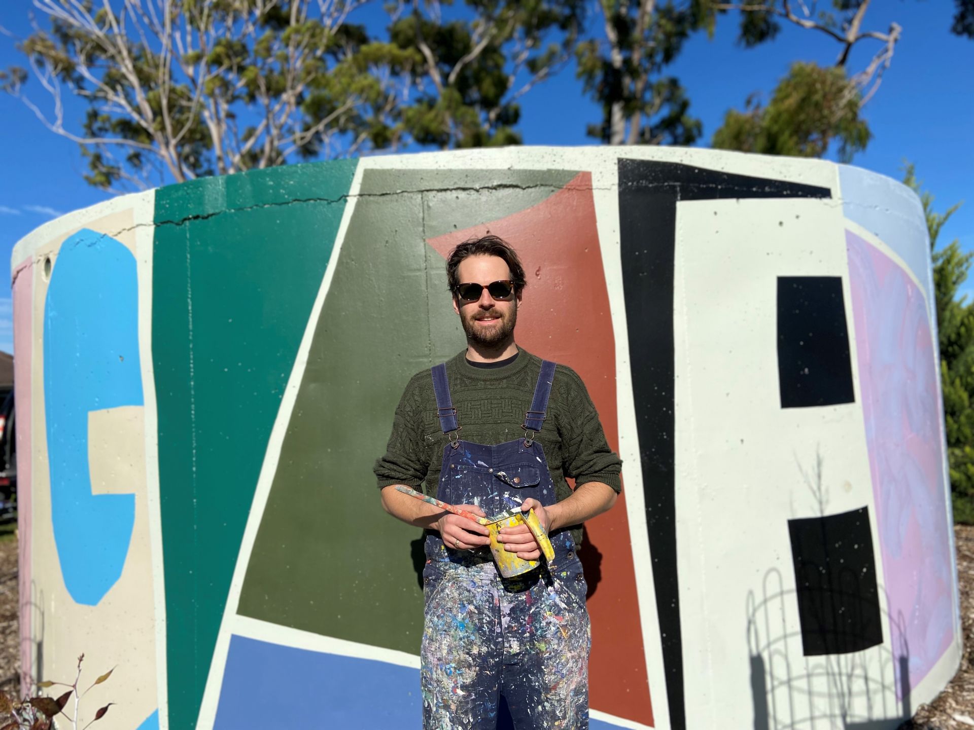 Together 2022 an abstract mural located on a water tank in Donald Street Reserve at St Marys with artist Tristan Kerr standing in front of the mural