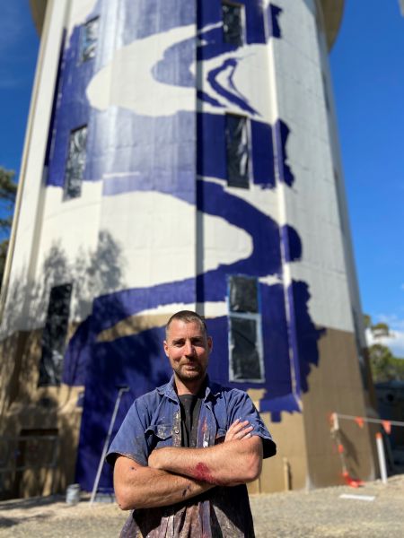Seb Humphries standing in front of his mural on the Belair Water Tower